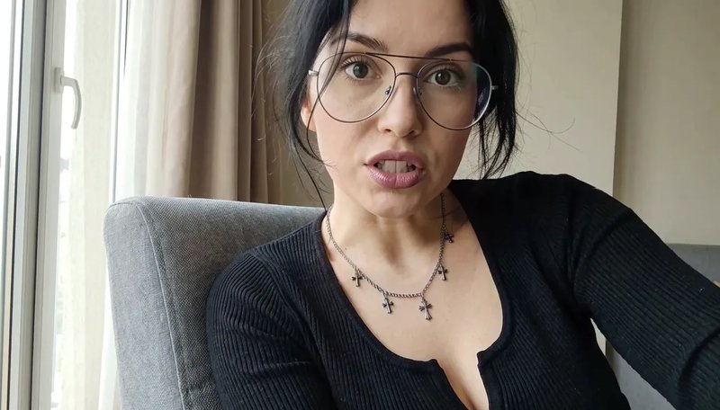 A woman in glasses speaking from a grey armchair